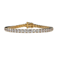 A yellow gold tennis bracelet featuring a continuous row of round-cut clear gemstones, displayed against a solid light beige background.