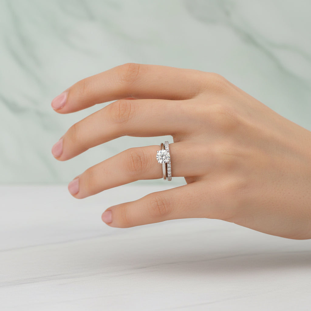 Hand wearing a silver ring with a diamond on a pink textured background