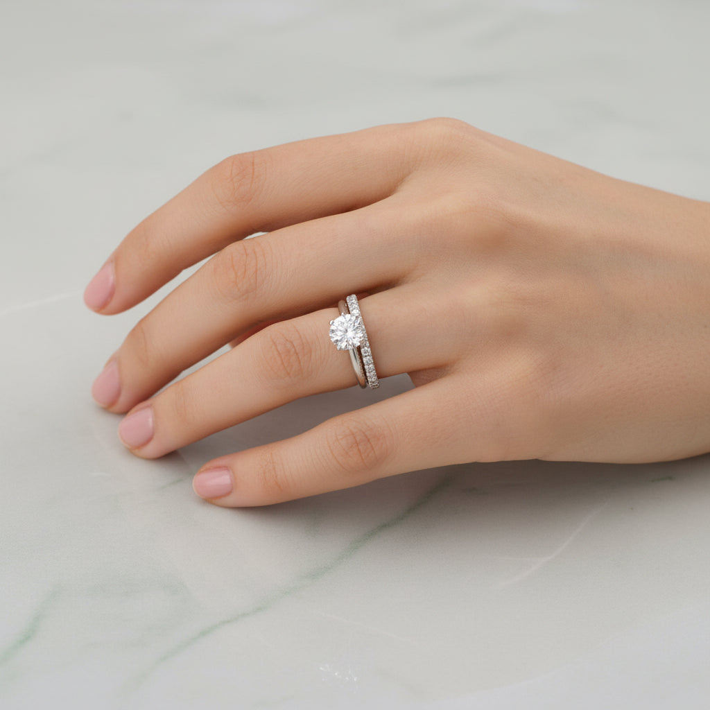 Hand wearing a silver ring with a diamond on a pink textured background