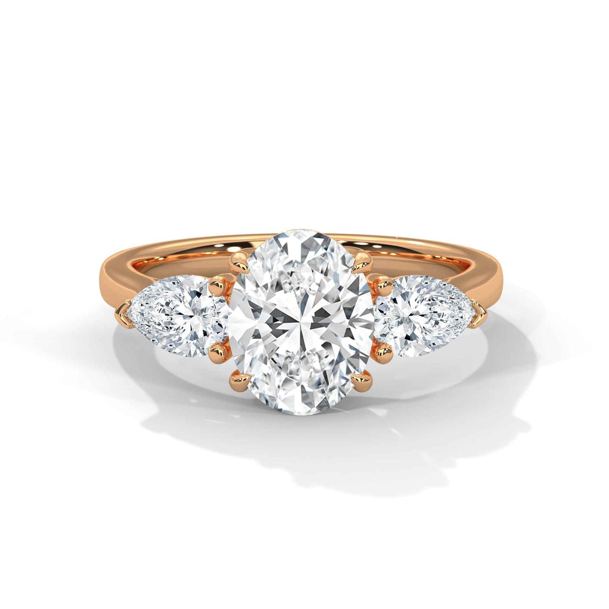 A rose gold three-stone engagement ring featuring a large oval center diamond flanked by two smaller round and pear-cut diamonds, set on a clean white background with a soft shadow.